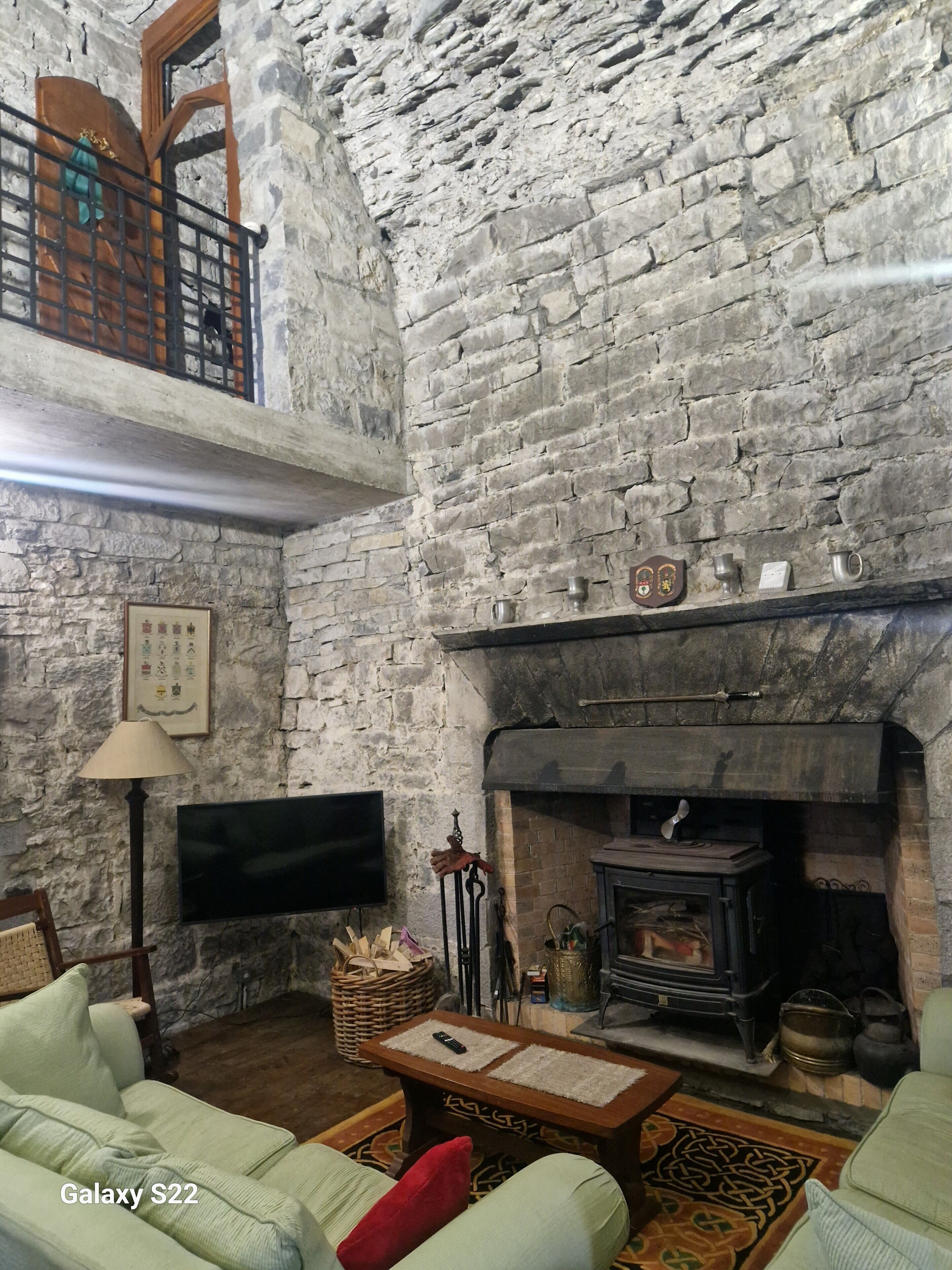 Un salon chaleureux avec un mur en pierre, une cheminée, un téléviseur et des sièges confortables.