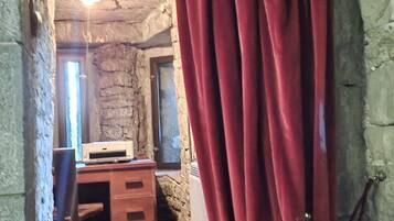A narrow stone-walled corridor with a wooden desk and drawers, a red curtain, and a hanging light fixture.