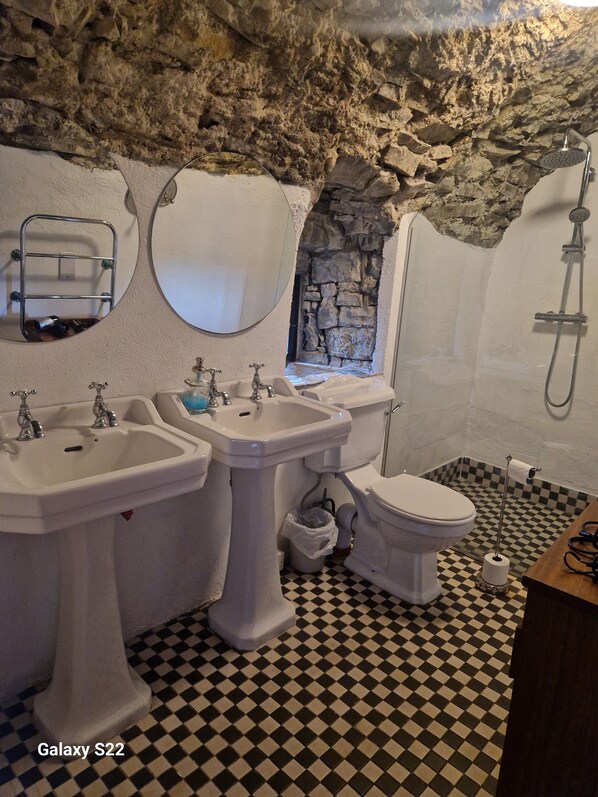 Un baño con piso a cuadros, dos lavamanos, un inodoro y una ducha.