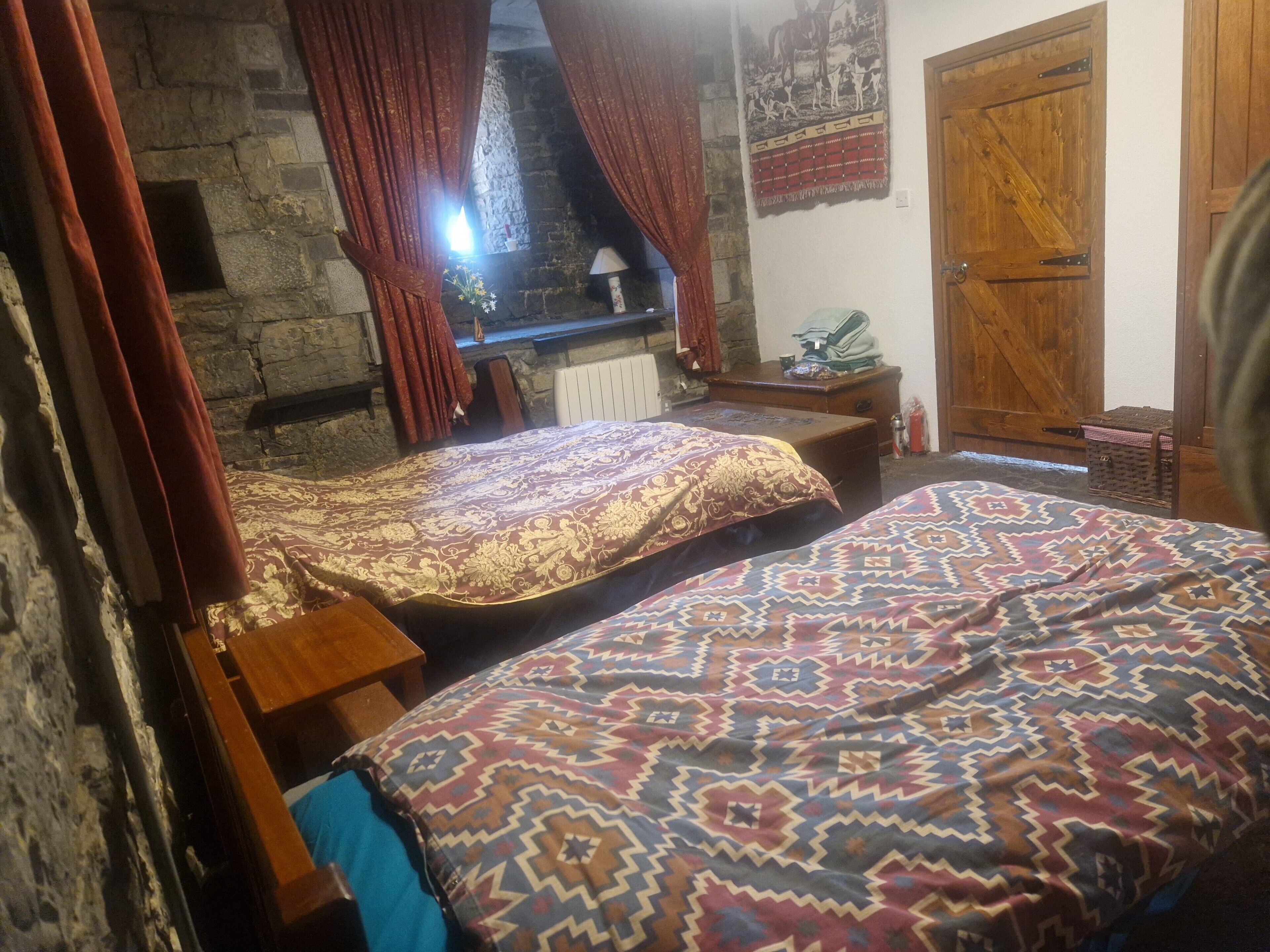 A room with two beds, a stone fireplace, a wooden door, and a stone wall.