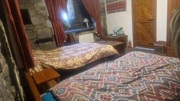 A room with two beds, a stone fireplace, a wooden door, and a stone wall.