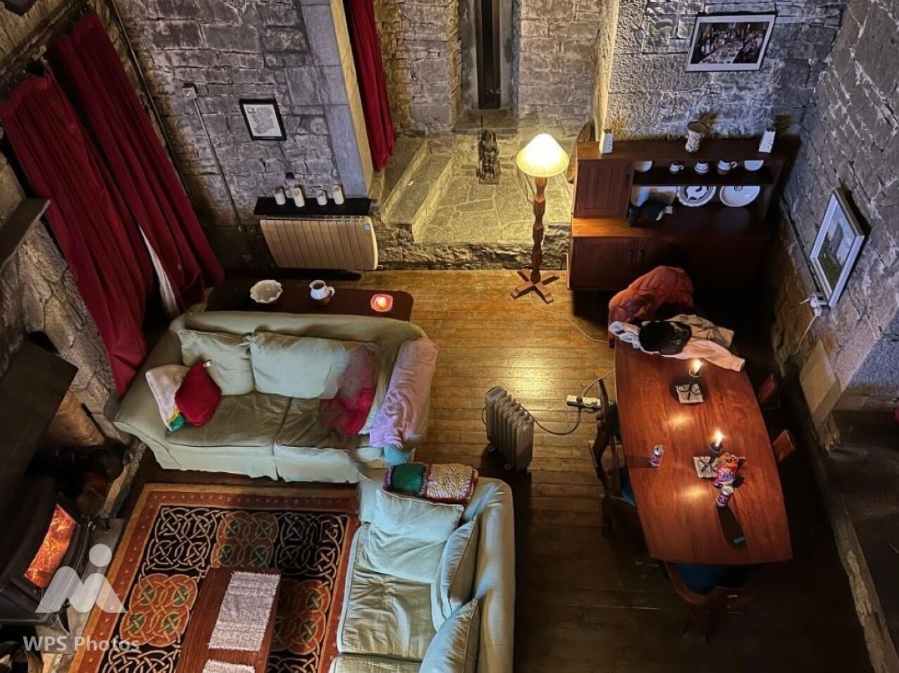 A cozy room with a stone wall, a wooden table, a sofa, and a red curtain.