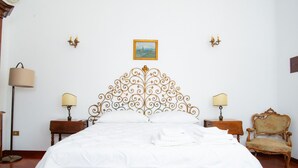 A neatly made bed with a decorative headboard, two bedside tables with lamps, a chair, and a painting on the wall.