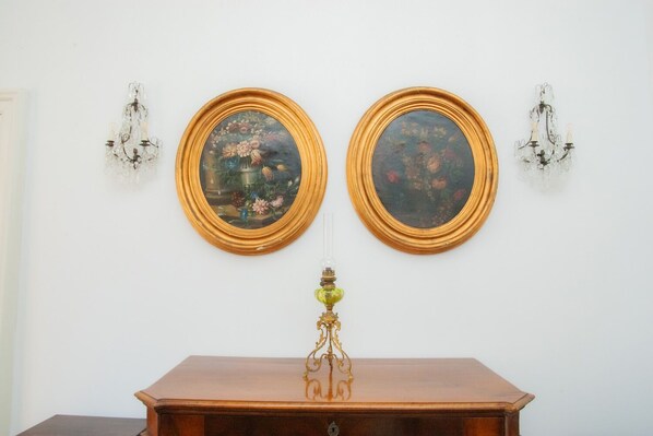 Two framed paintings on a wall, a wooden table with a lamp in front, and wall sconces on either side. - San Pasquale 62 Apartment (NAPOLI)