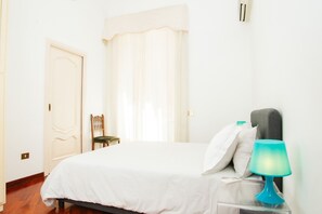 A bedroom with a bed, a chair, a nightstand with a lamp, a window with curtains, and a door. - San Pasquale 62 Apartment (NAPOLI)