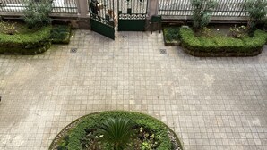 A paved courtyard with a circular garden, a metal fence, and a gate.
