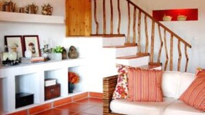 A cozy living room with a wooden staircase, a sofa with cushions, and a coffee table with decorative items. - Partridge House (Coruche)