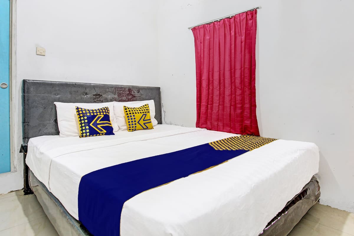 A bed with a white mattress, blue and yellow pillows, and a red curtain.