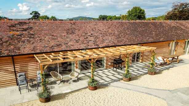 Een overdekt terras met buitenmeubels, een pergola en planten in potten.