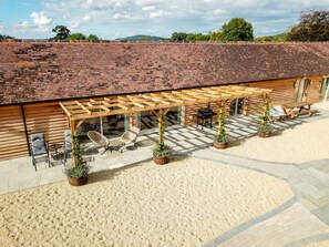 A covered patio area with outdoor seating, a pergola, and potted plants. - Luxury 3-Bed Cotswolds Barn for Families & Friends (Gloucester)