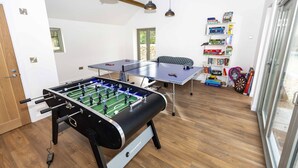 Een kamer met een tafelvoetbaltafel, een pingpongtafel en een boekenplank met diverse spullen.