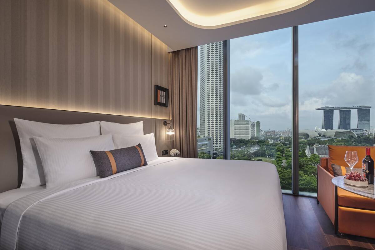 Habitación de hotel moderna con una cama grande, un escritorio con silla y vistas a edificios de la ciudad.
