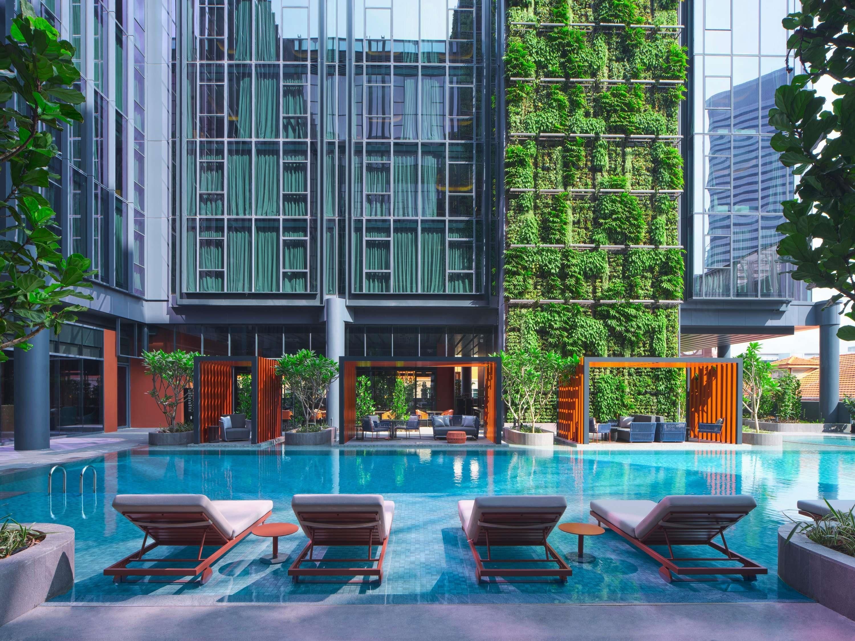 A modern building with a glass facade, a rooftop garden, and a swimming pool with lounge chairs.