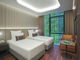 Habitación de hotel moderna con dos camas, una mesita con manzanas y vistas a zonas verdes a través de grandes ventanales.