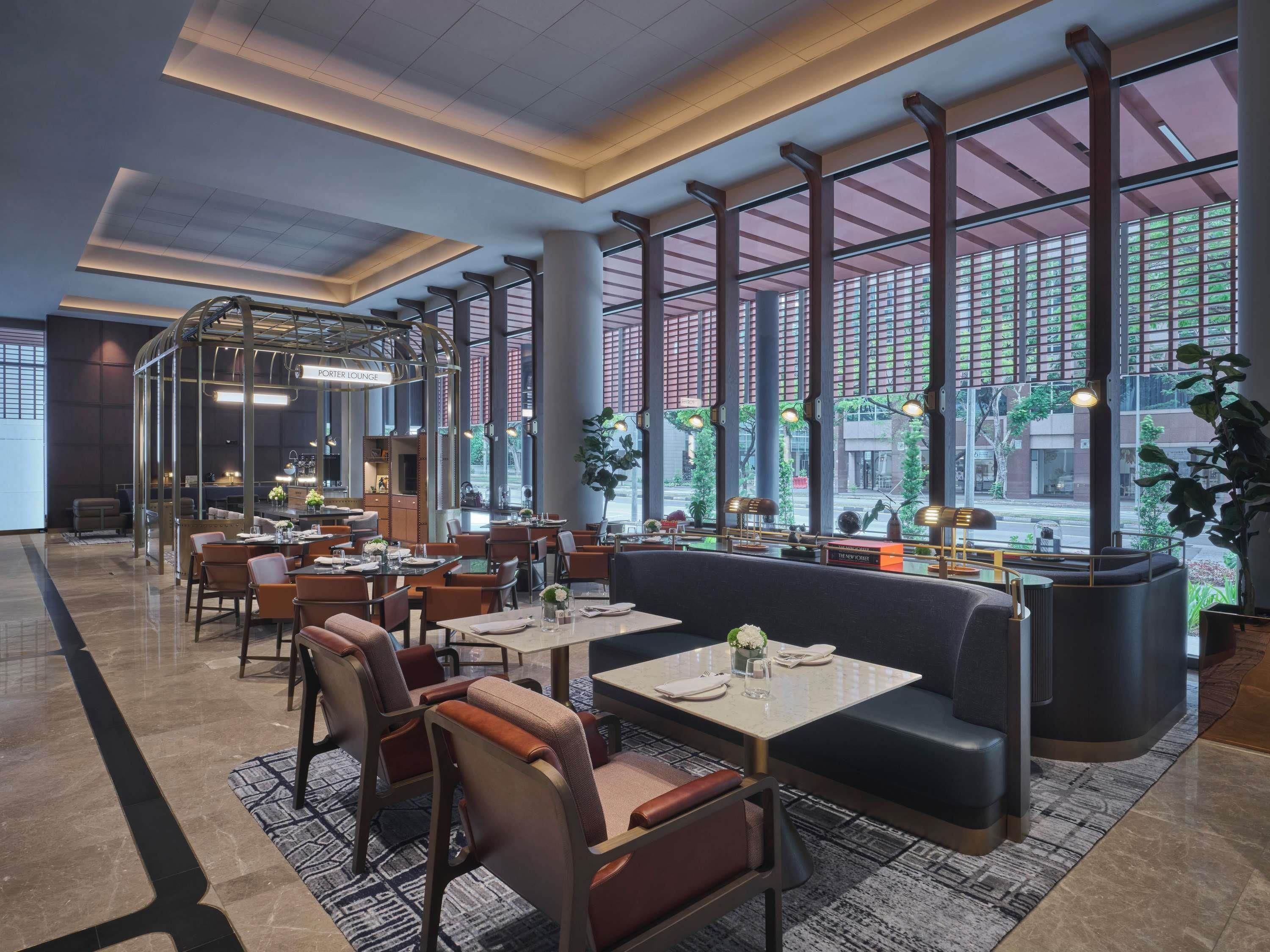 Un restaurante moderno con techos altos, ventanas amplias y diversas opciones de asientos, incluyendo mesas y cabinas.