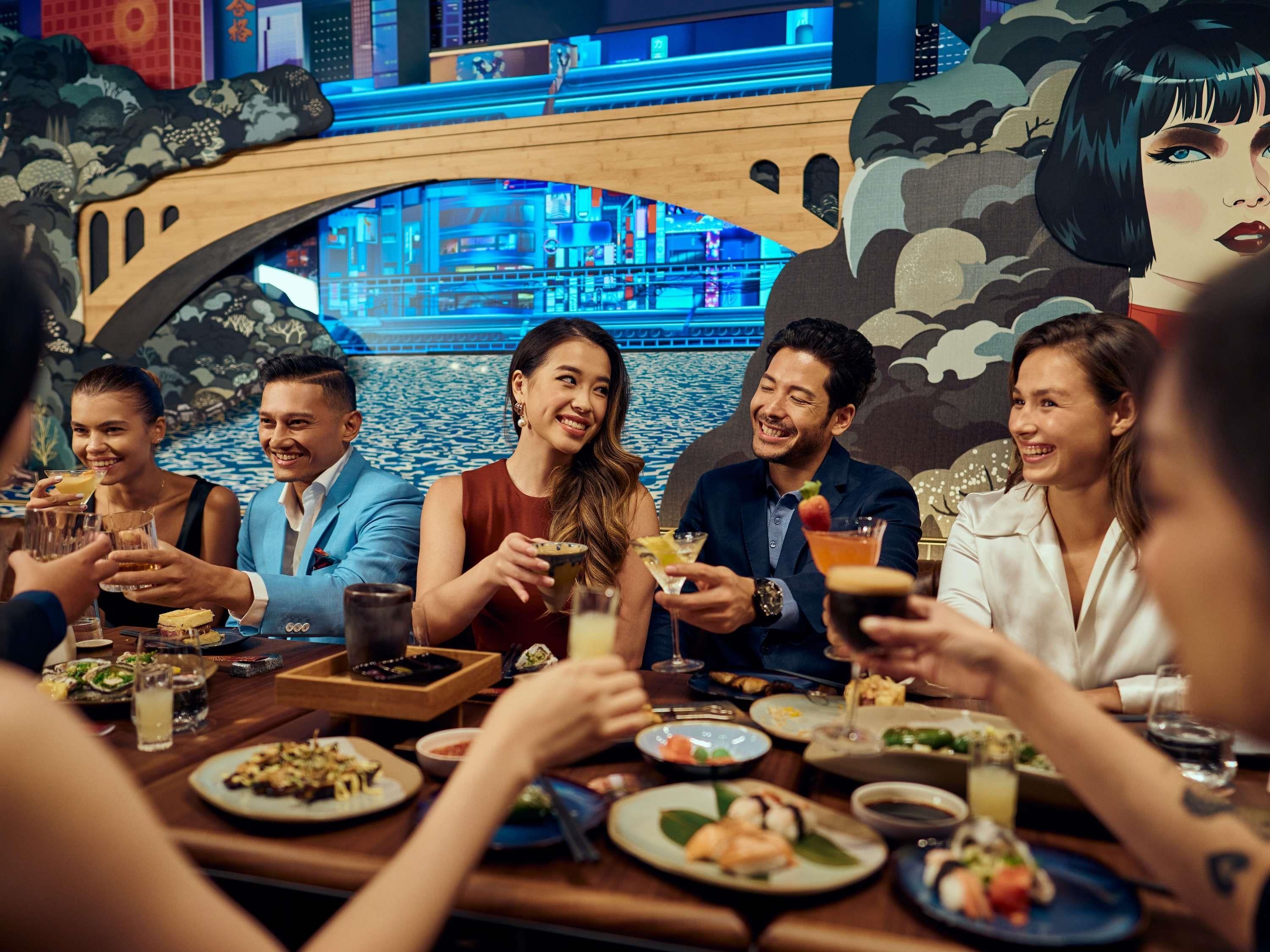 A group of people dining at a restaurant with a view of a bridge and a mural.