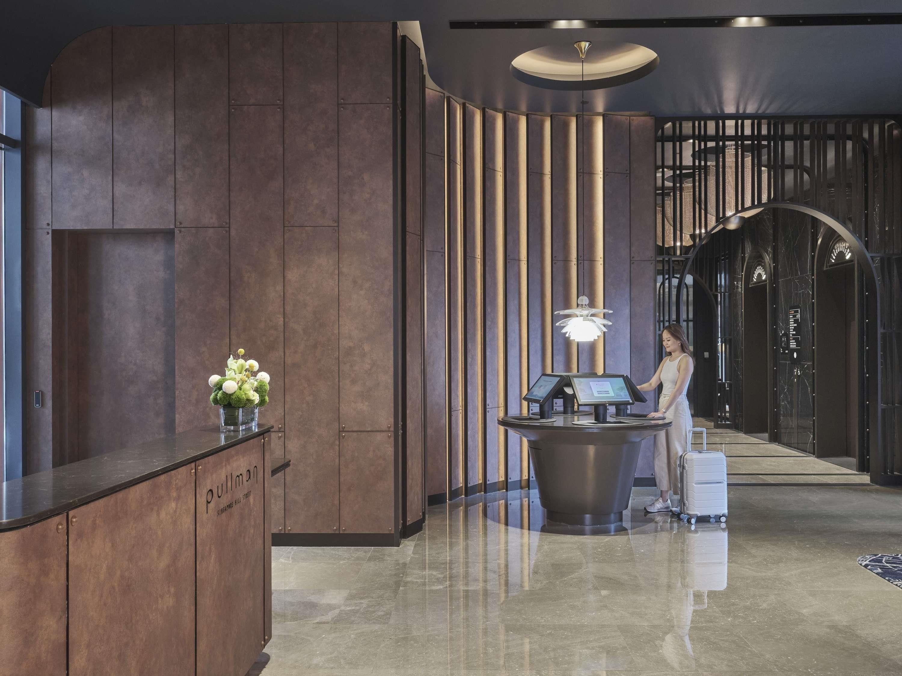 A reception area with a modern design, featuring a reception desk, a digital information kiosk, and a decorative vase with flowers.