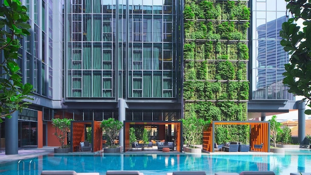 A modern building with a glass facade, a rooftop garden, and a swimming pool with lounge chairs. - Pullman Singapore Hill Street (Singapore)