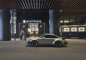A silver sports car parked in front of a building with a 'pullman' sign.