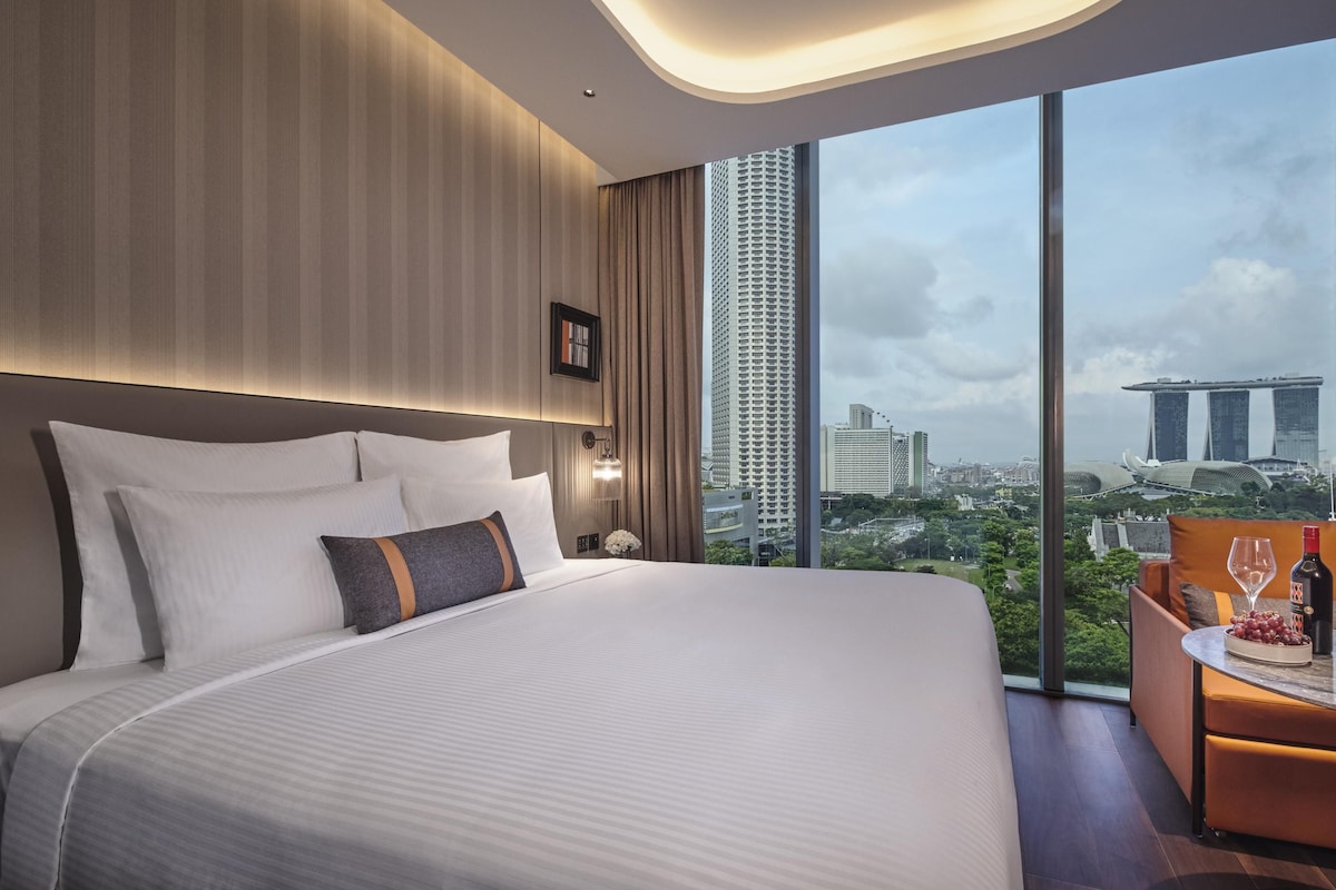 Une chambre d’hôtel moderne avec un grand lit, un bureau avec une chaise et une vue sur les bâtiments de la ville.