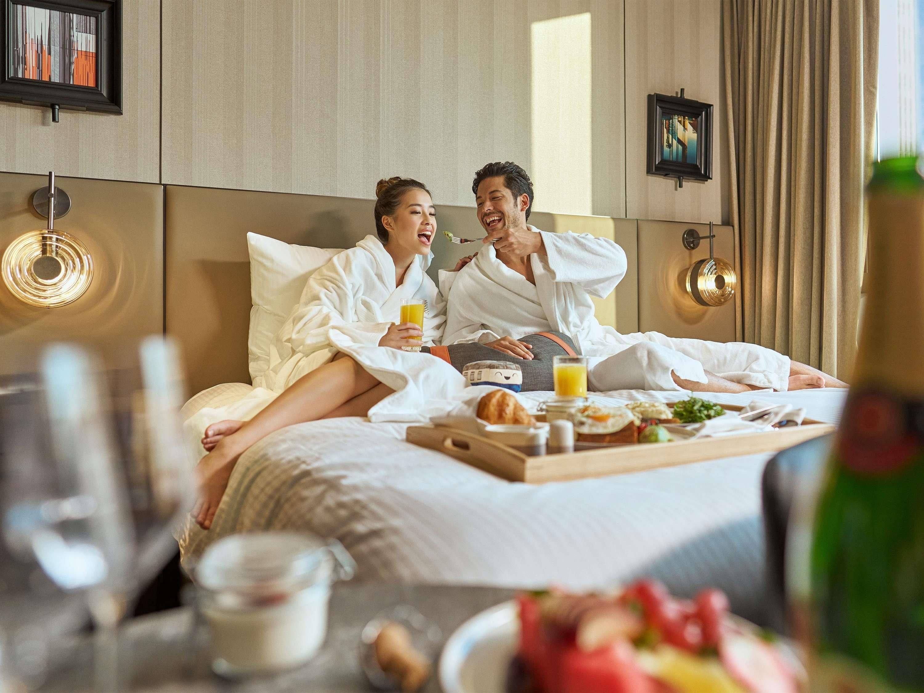 A hotel room with a bed, a tray with breakfast items, and a bedside table with a glass of orange juice.