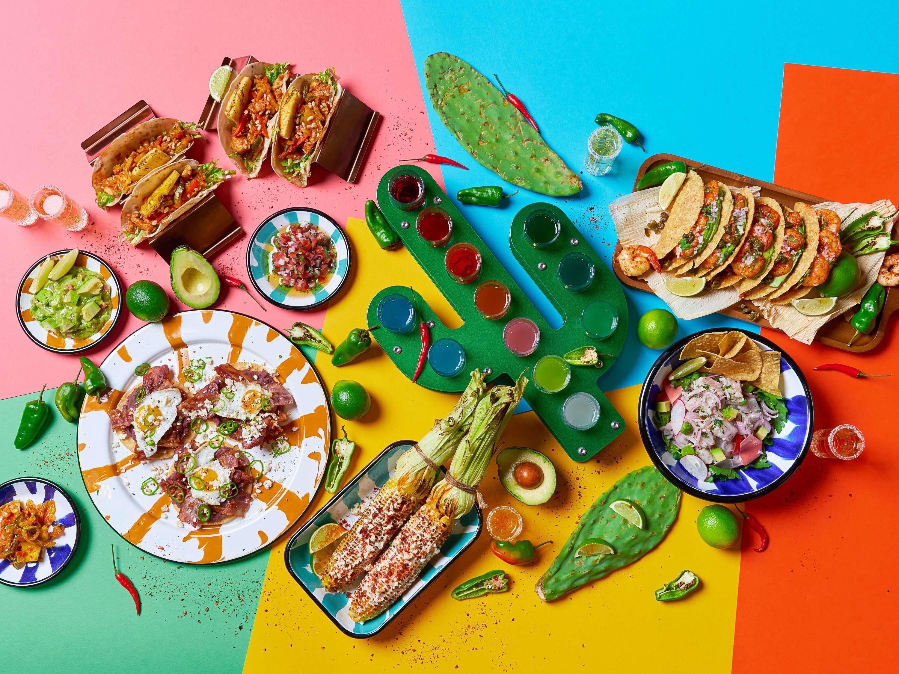 A colorful food arrangement with tacos, guacamole, and corn on the cob.
