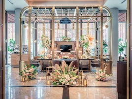 Un área de recepción con diseño moderno, que incluye un mostrador central, zona de estar y arreglos florales decorativos.