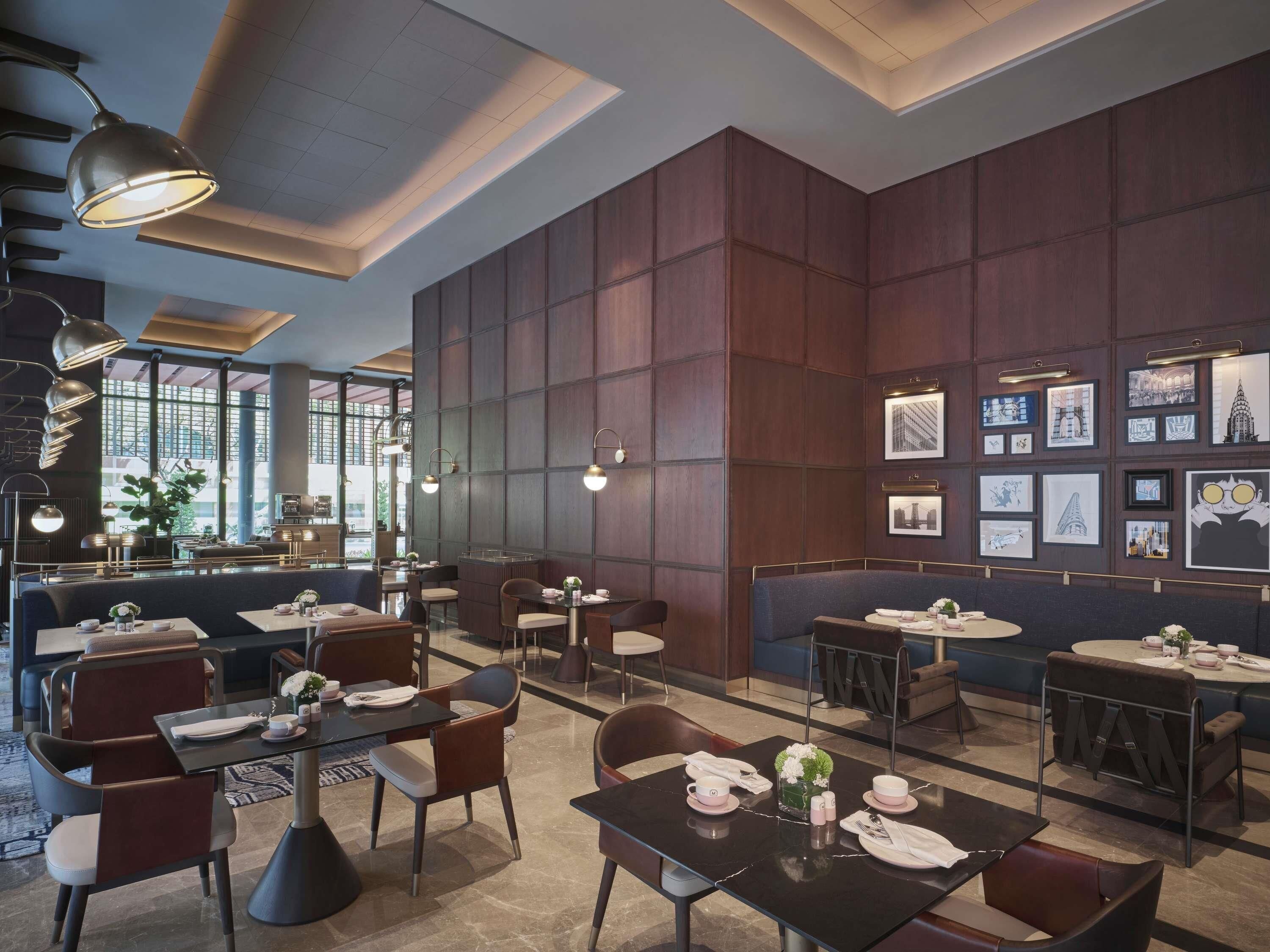 Un restaurante moderno con techos altos, iluminación colgante y diversas opciones de asientos, incluyendo cabinas y mesas.