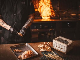 Eine Person bereitet Essen mit einem Grill und einem Spießbräter zu.