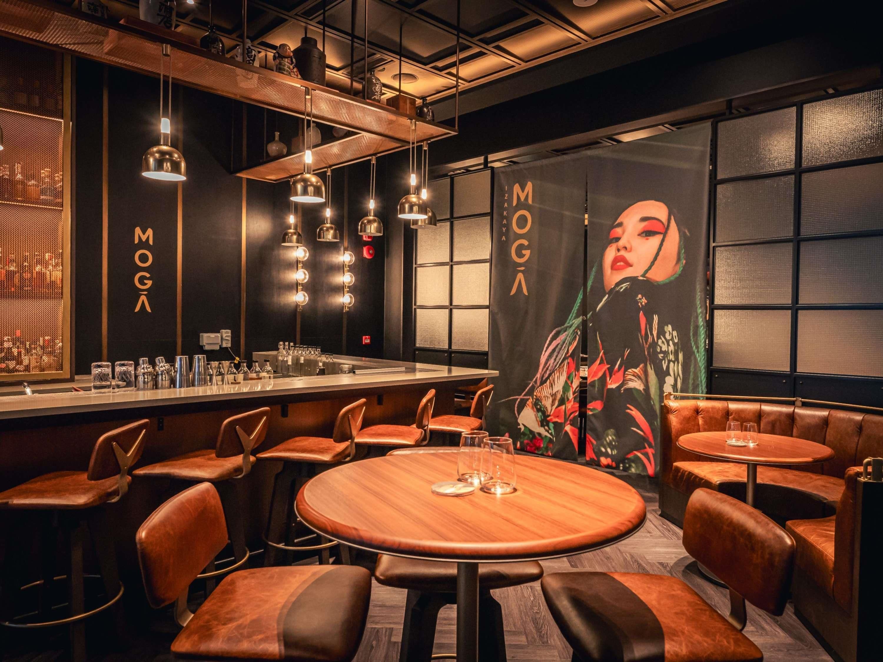 A bar area with round tables, leather booths, and hanging pendant lights.