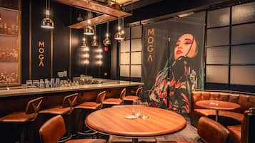 A bar area with round tables, leather booths, and hanging pendant lights.