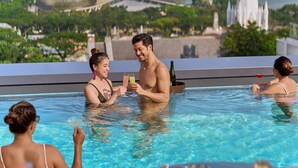 A poolside area with a table set for dining, a view of the Singapore skyline, and people enjoying the pool. - Pullman Singapore Hill Street (Singapore)