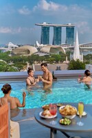 Ein Poolbereich mit Esstisch, Blick auf den Singapurer Skyline und Personen, die das Schwimmbad nutzen.