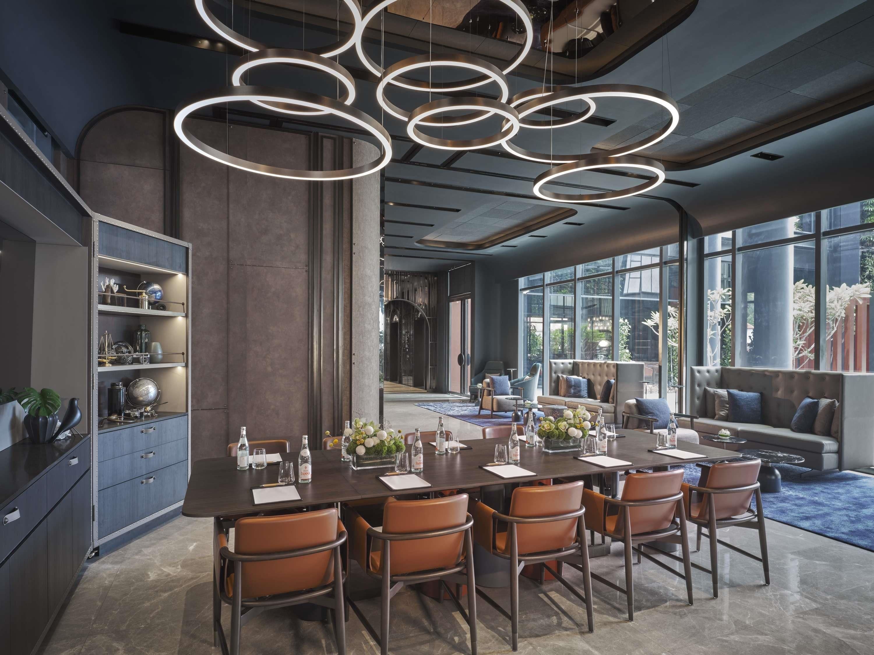 A modern dining area with a long table, chairs, and overhead circular lighting.