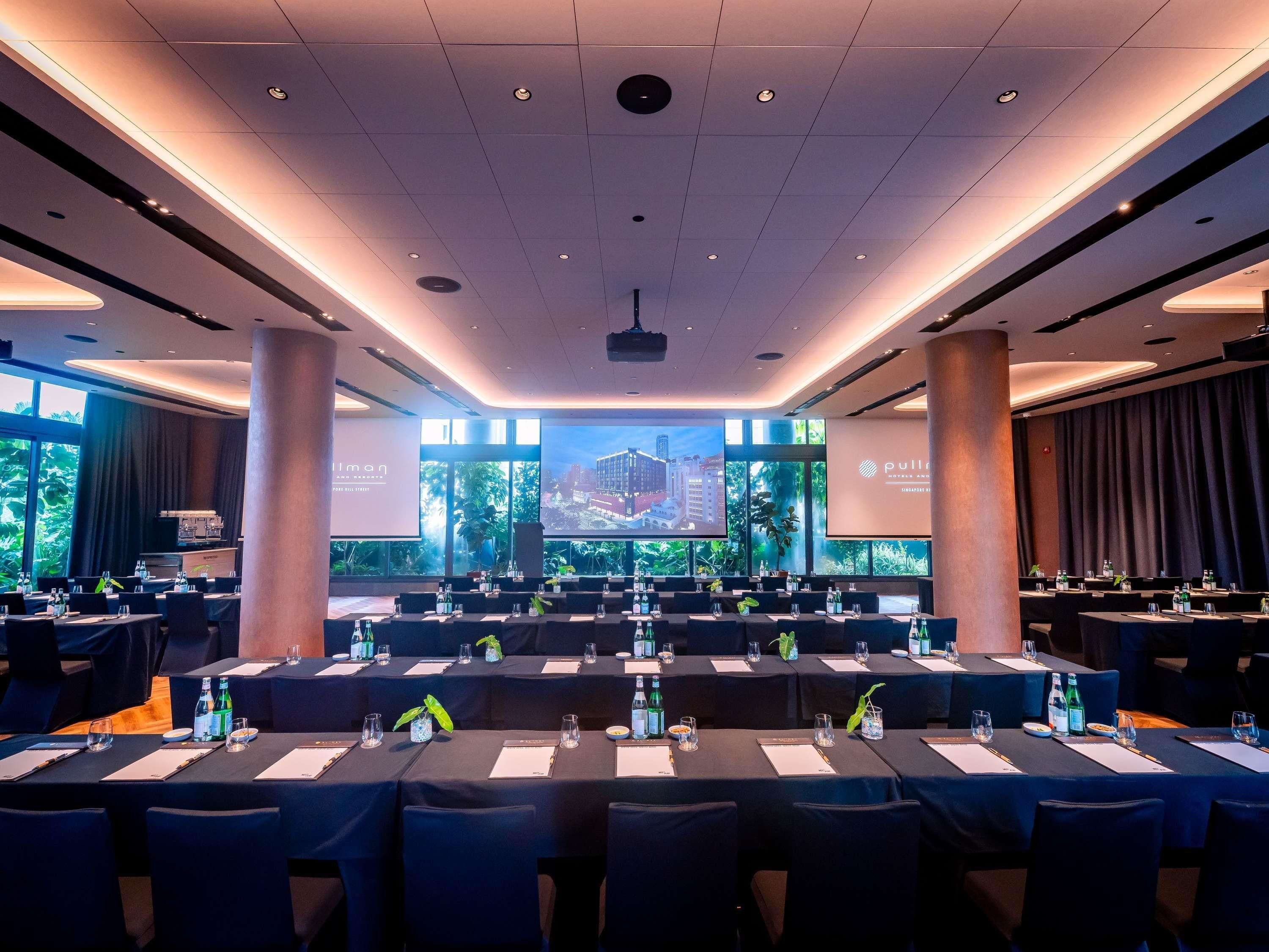 A conference room with tables set for a meeting, large windows with a cityscape view, and a presentation screen.
