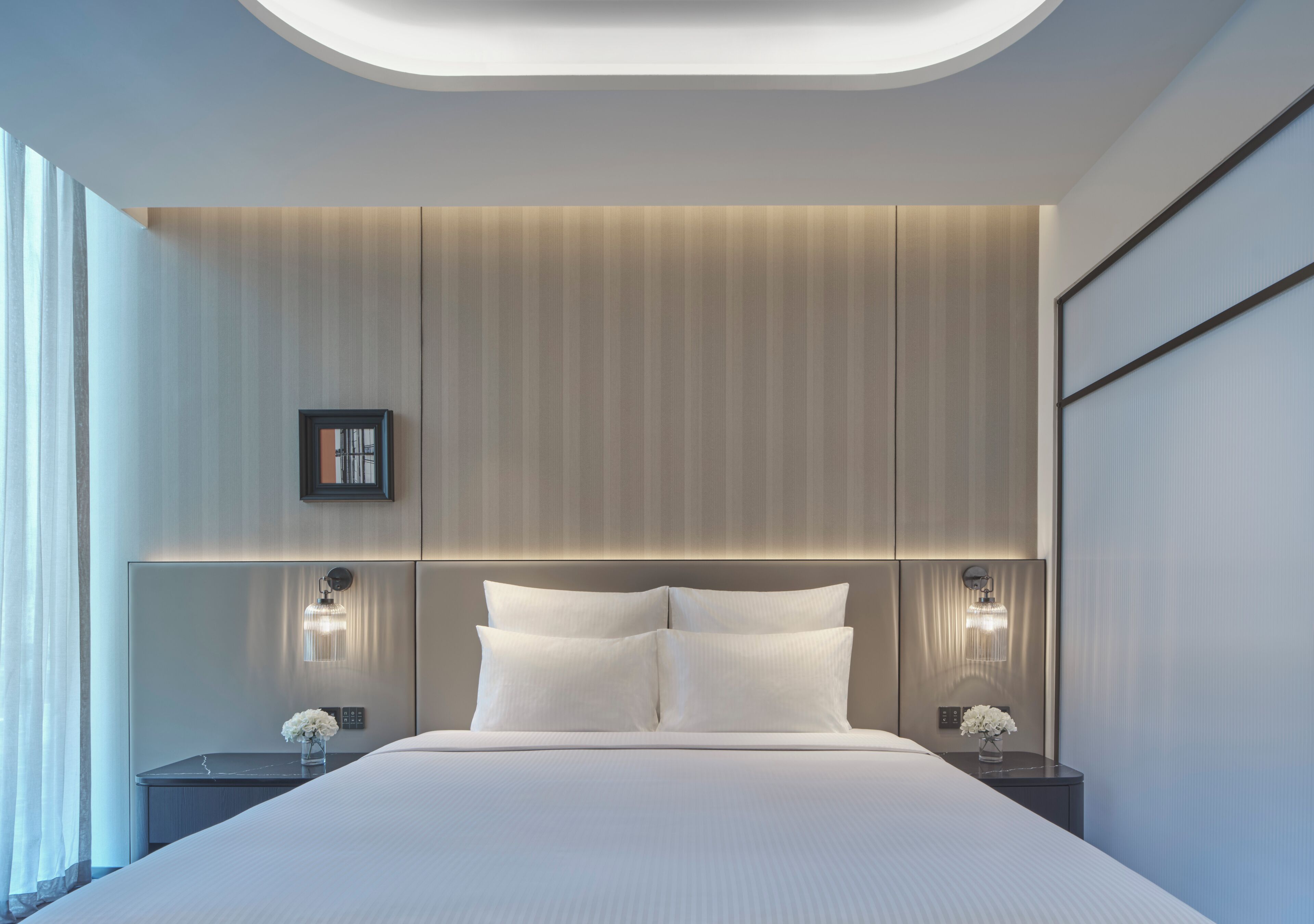 A modern hotel room with a large bed, two bedside tables with lamps, and a wall-mounted light fixture.