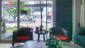 A hotel lobby with wicker chairs, a small table with a plant, and a view of the street outside. - OYO 3216 Ellegan Residence (South Tangerang)