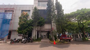 A modern building with a glass entrance, surrounded by trees and parked vehicles. - OYO 3216 Ellegan Residence (South Tangerang)