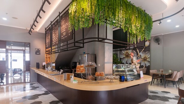A modern cafe with a curved counter, a menu board, and a hanging green plant. - OYO 3216 Ellegan Residence (South Tangerang)