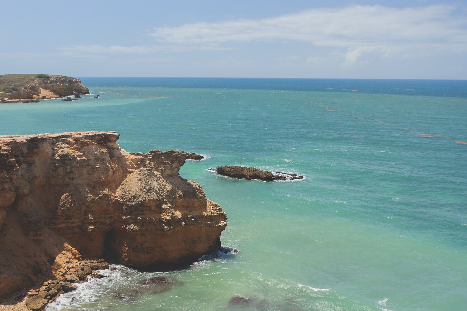 A coastal landscape with a prominent cliff and clear turquoise waters.