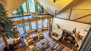 A spacious loft with a high ceiling, large windows, a cozy seating area with a fireplace, and various decorative animal heads. - Little River Lodge sleeps 12 (Fort Payne)