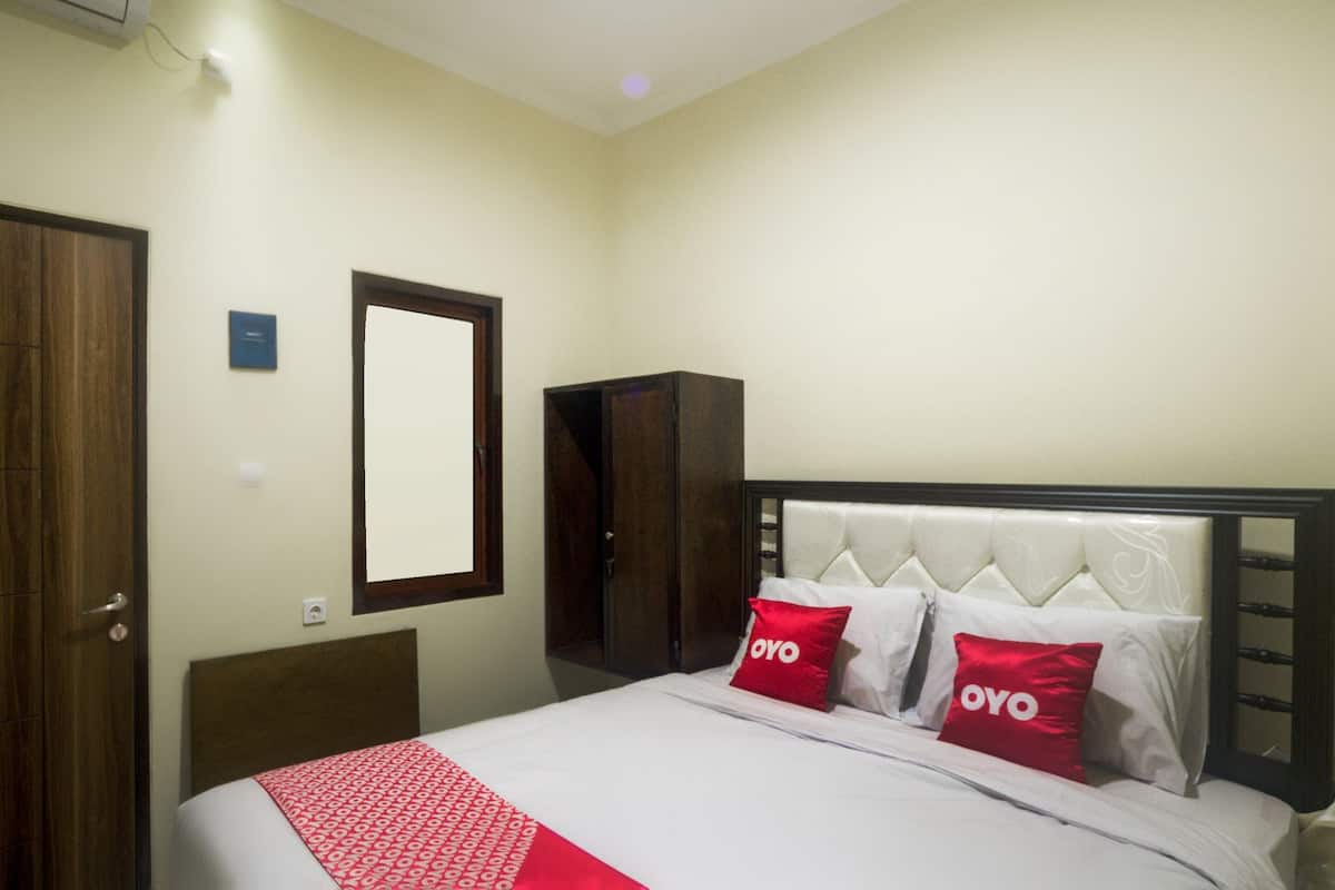 A hotel room with a bed, two red pillows with "OYO" branding, a wooden wardrobe, and a mirror on the wall.