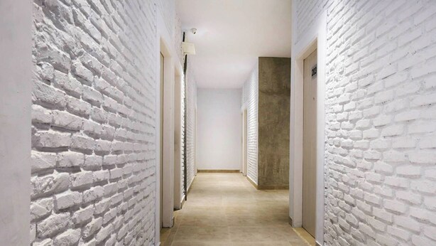 Un couloir étroit aux murs en briques blanches et au sol carrelé de couleur beige.