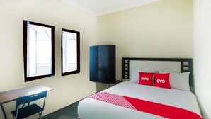 Une chambre d’hôtel avec un lit, deux fenêtres, un bureau et une armoire.