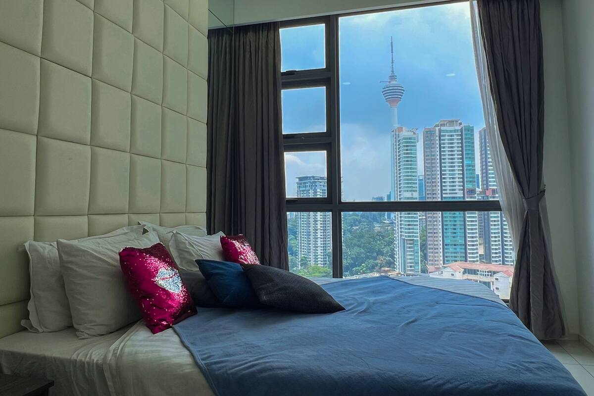 Une chambre à coucher avec un grand lit, une tête de lit capitonnée et une vue sur le paysage urbain, avec une tour en particulier.