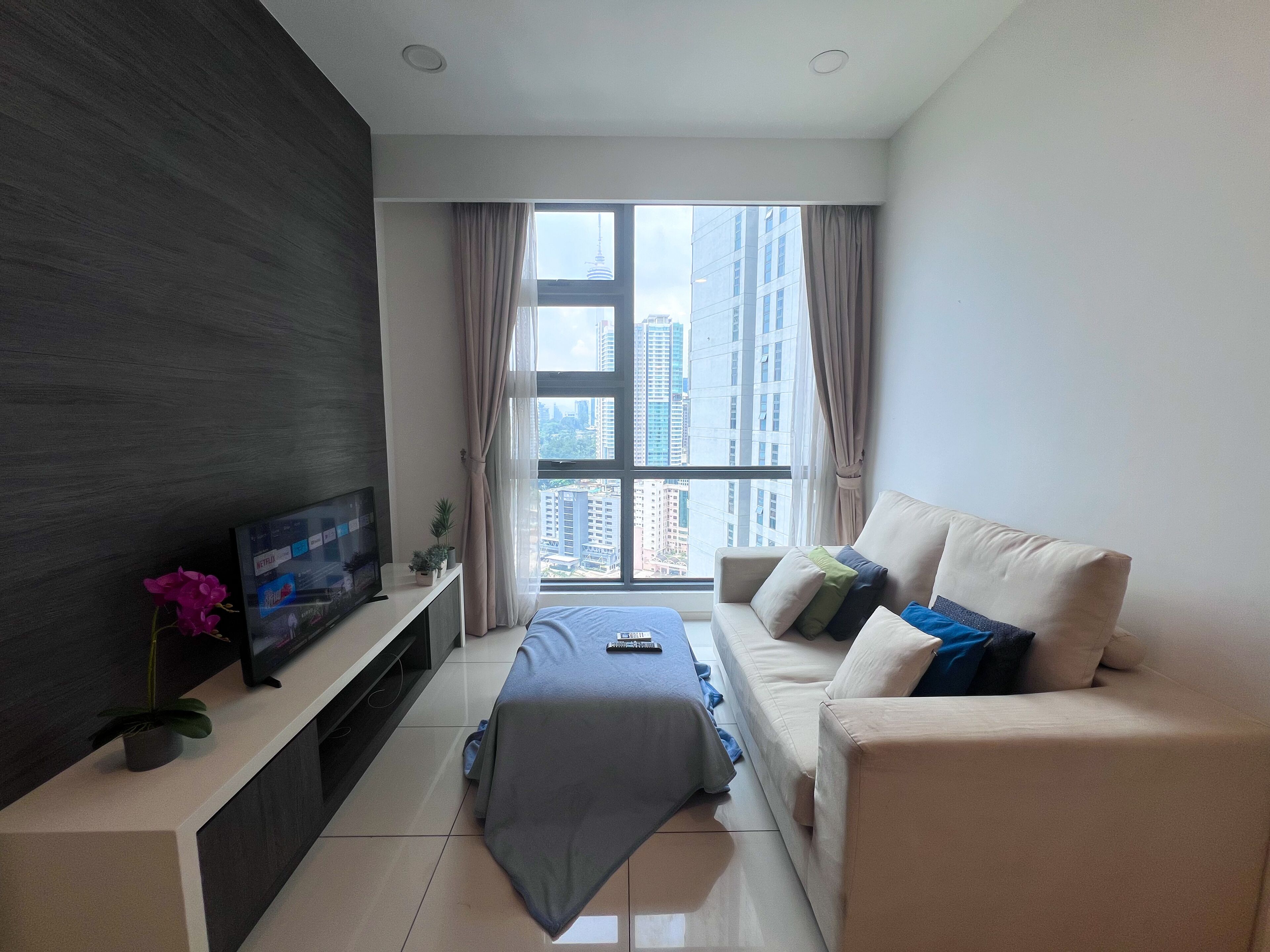 A modern bedroom with a large window, a flat-screen TV, a bed, and a sofa.
