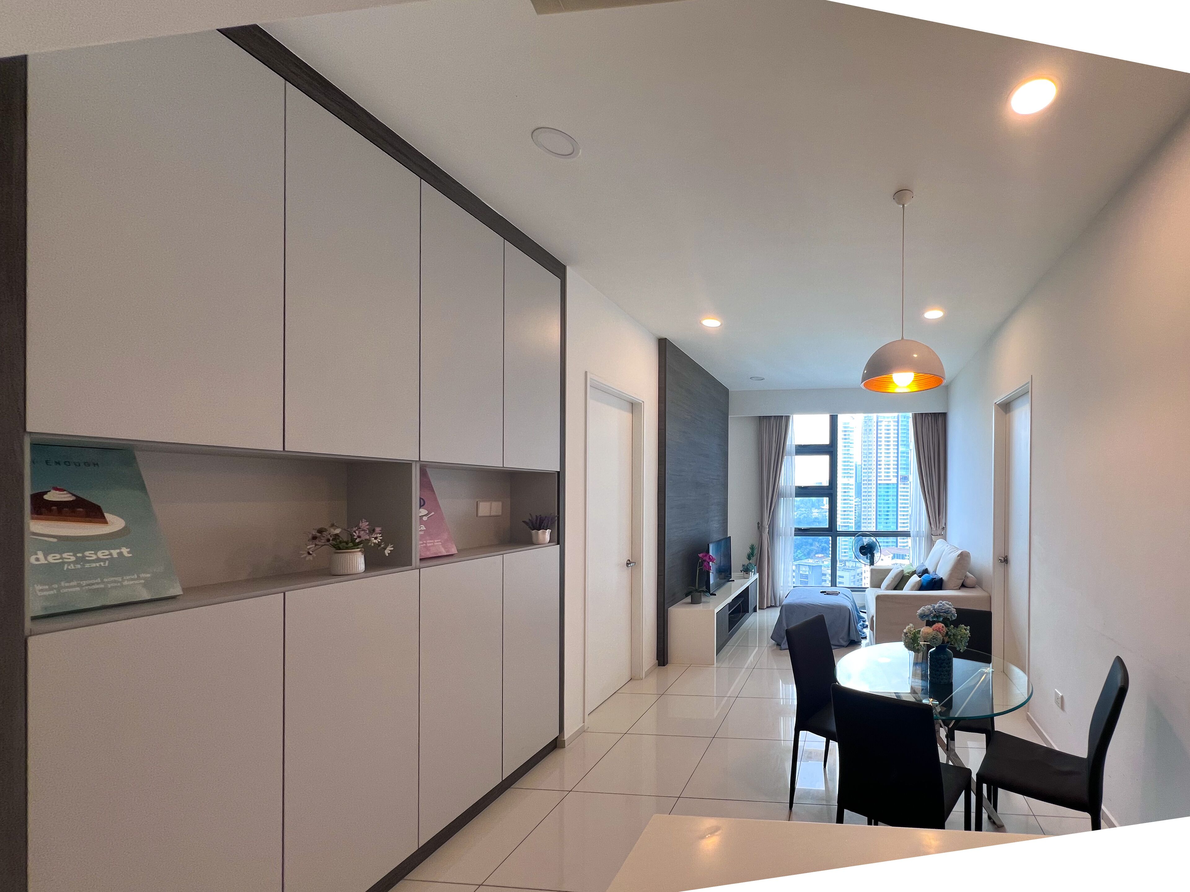 A modern kitchen with white cabinets, a dining area with a glass table, and a view of tall buildings outside.