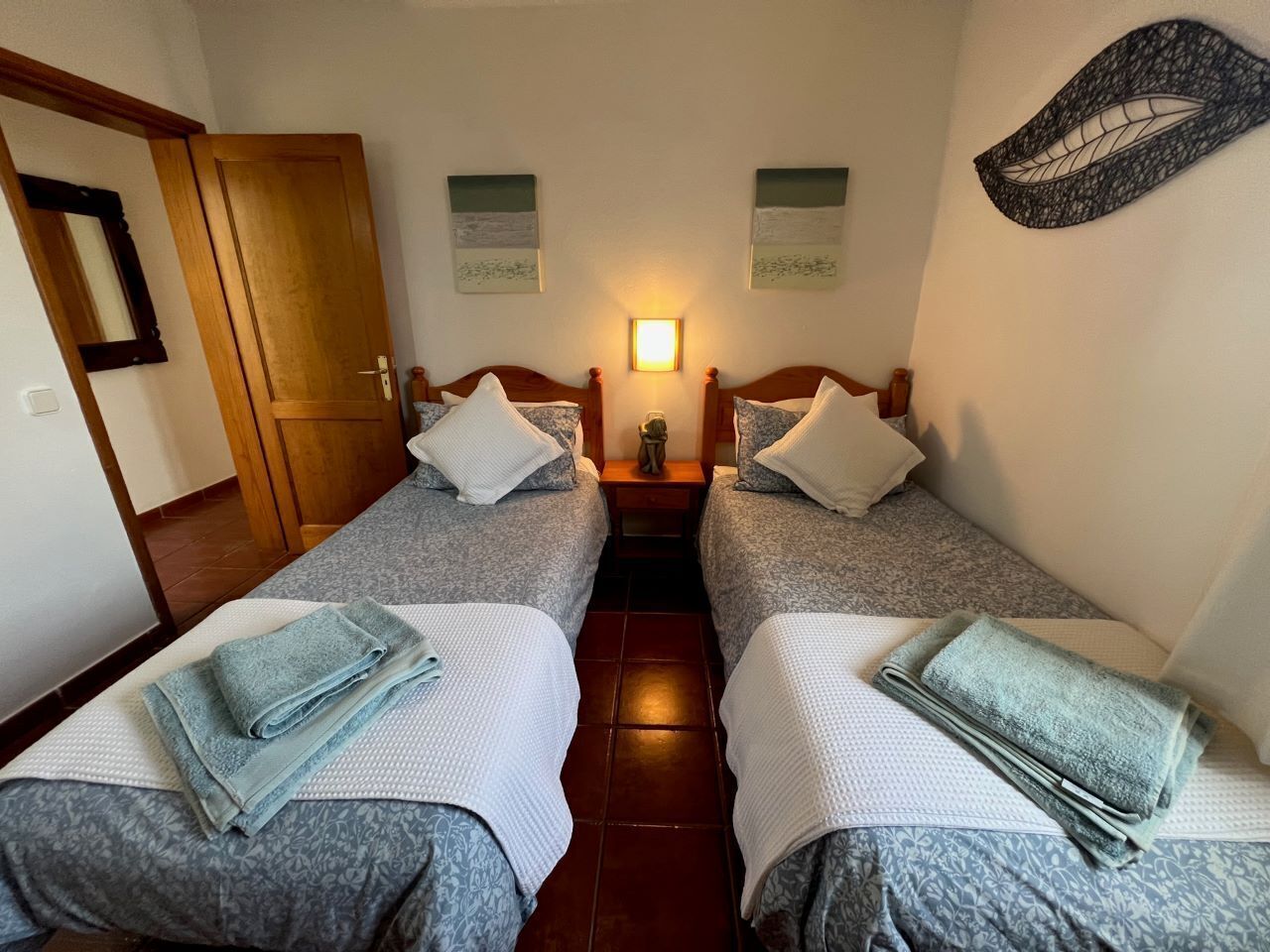 A room with two single beds, a nightstand between them, and a wall-mounted lamp.