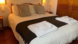 Ein ordentlich bezogenes Bett mit einer schwarzen Tagesdecke und weißen Handtüchern, ein Holzschrank und zwei Nachttische mit Lampen.