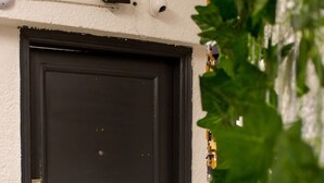 Une porte de couleur sombre, dotée d’une poignée en laiton et d’un trou de serrure, est encastrée dans un mur blanc, au-dessus duquel est fixée une petite caméra de surveillance.
